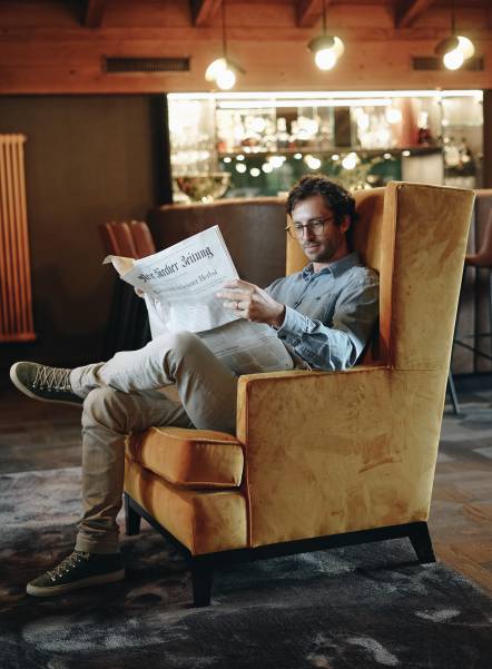 Mann liest Zeitung in Sessel Cocktailbar Naturhotel Forsthofgut