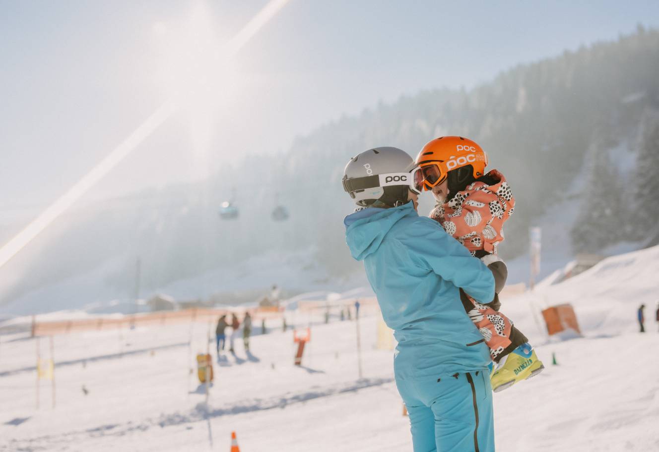 Person hält Kind auf den Armen im Skigebiet