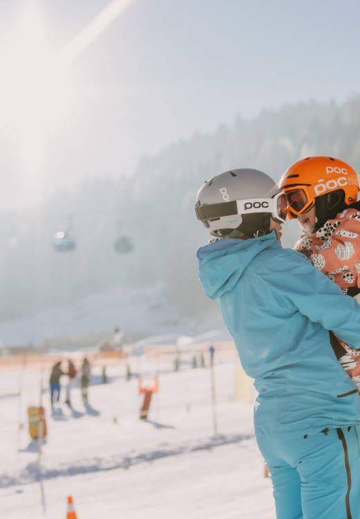 Person hält Kind auf den Armen im Skigebiet